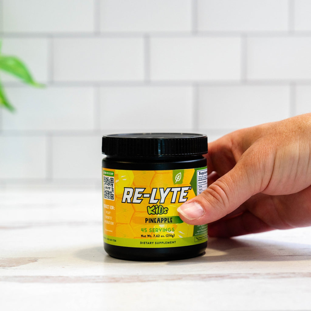 Hand holds a black jar of Re-Lyte Kids Pineapple dietary supplement.