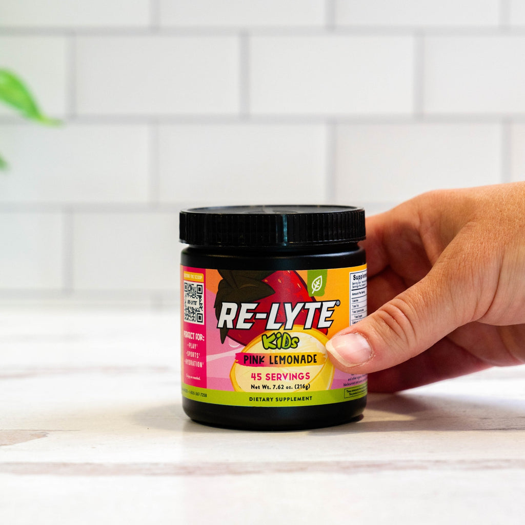 Hand holds a jar of Re-Lyte Kids Pink Lemonade dietary supplement.