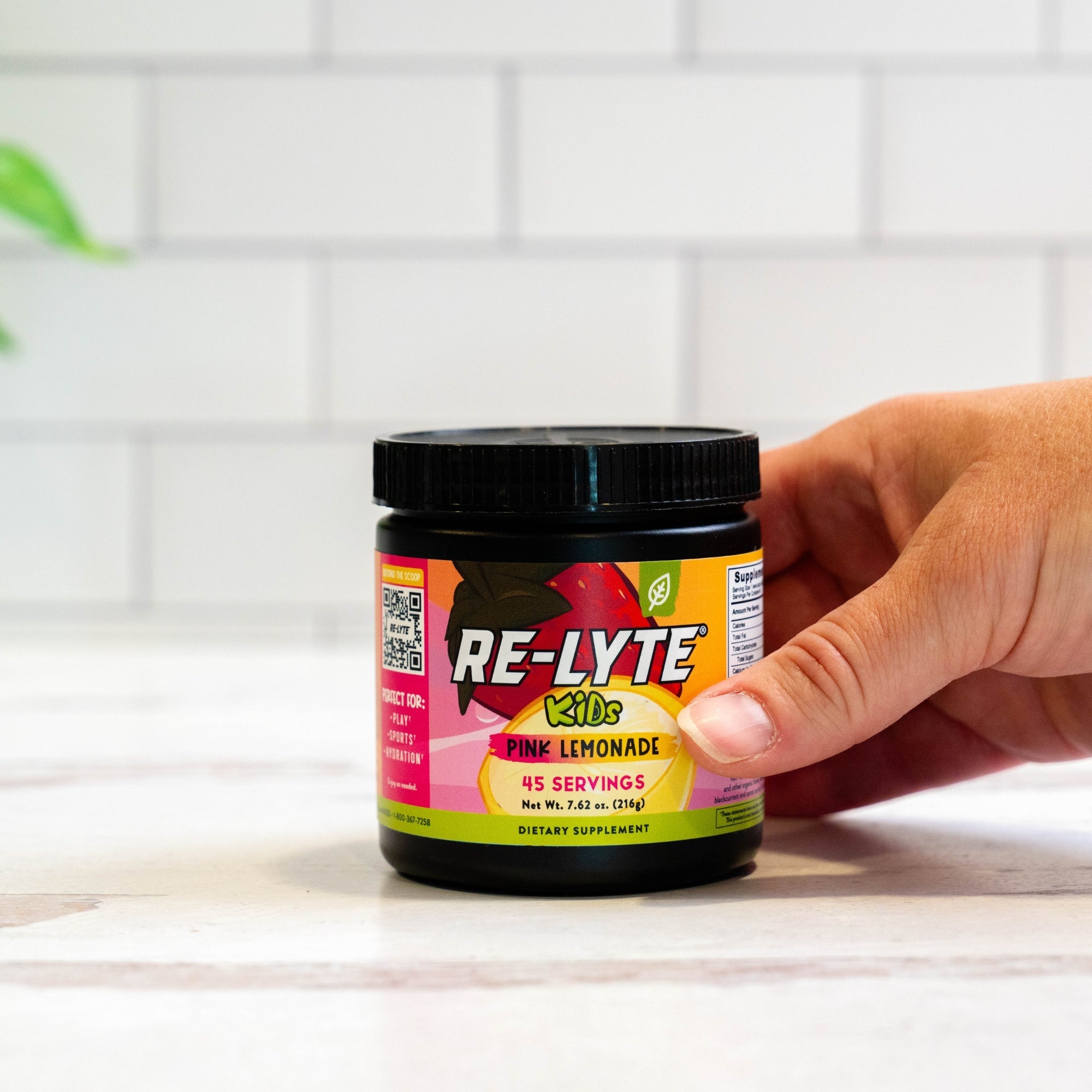 Hand holds a jar of Re-Lyte Kids Pink Lemonade dietary supplement.