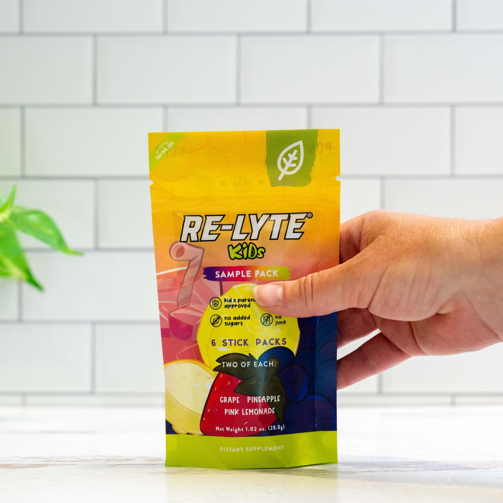Hand holds a Re-Lyte Kids Sample Pack of electrolyte powder, showcasing the yellow packaging and its three flavors: grape, pineapple, and pink lemonade.